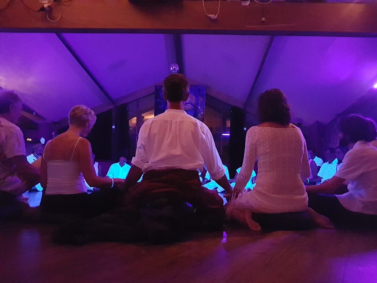 Personas sentadas en círculo, de espaldas y tomadas de la mano, bajo una luz violeta