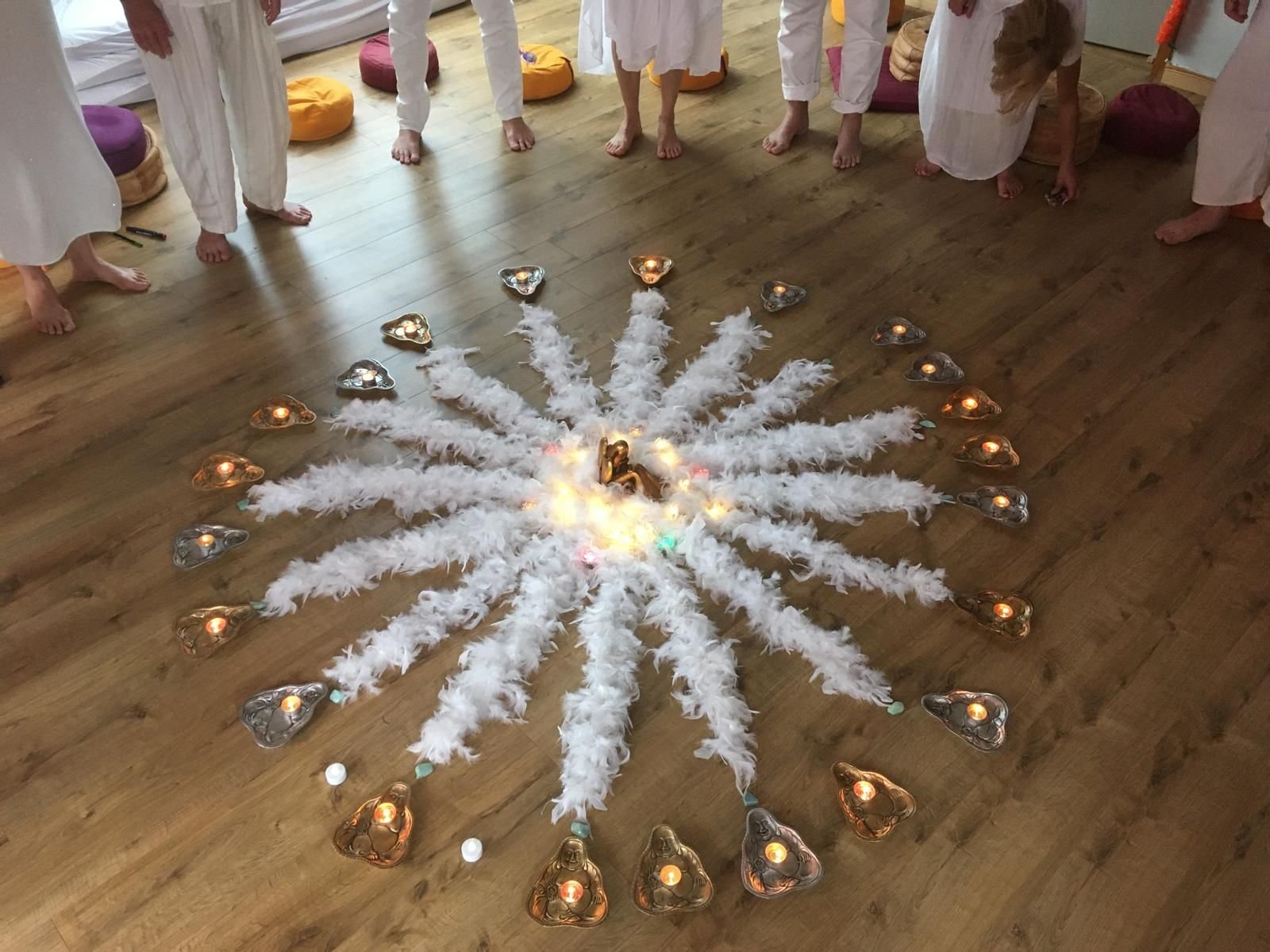 Mandala de plumas blancas y velas en el suelo, rodeado por los pies descalzos del grupo