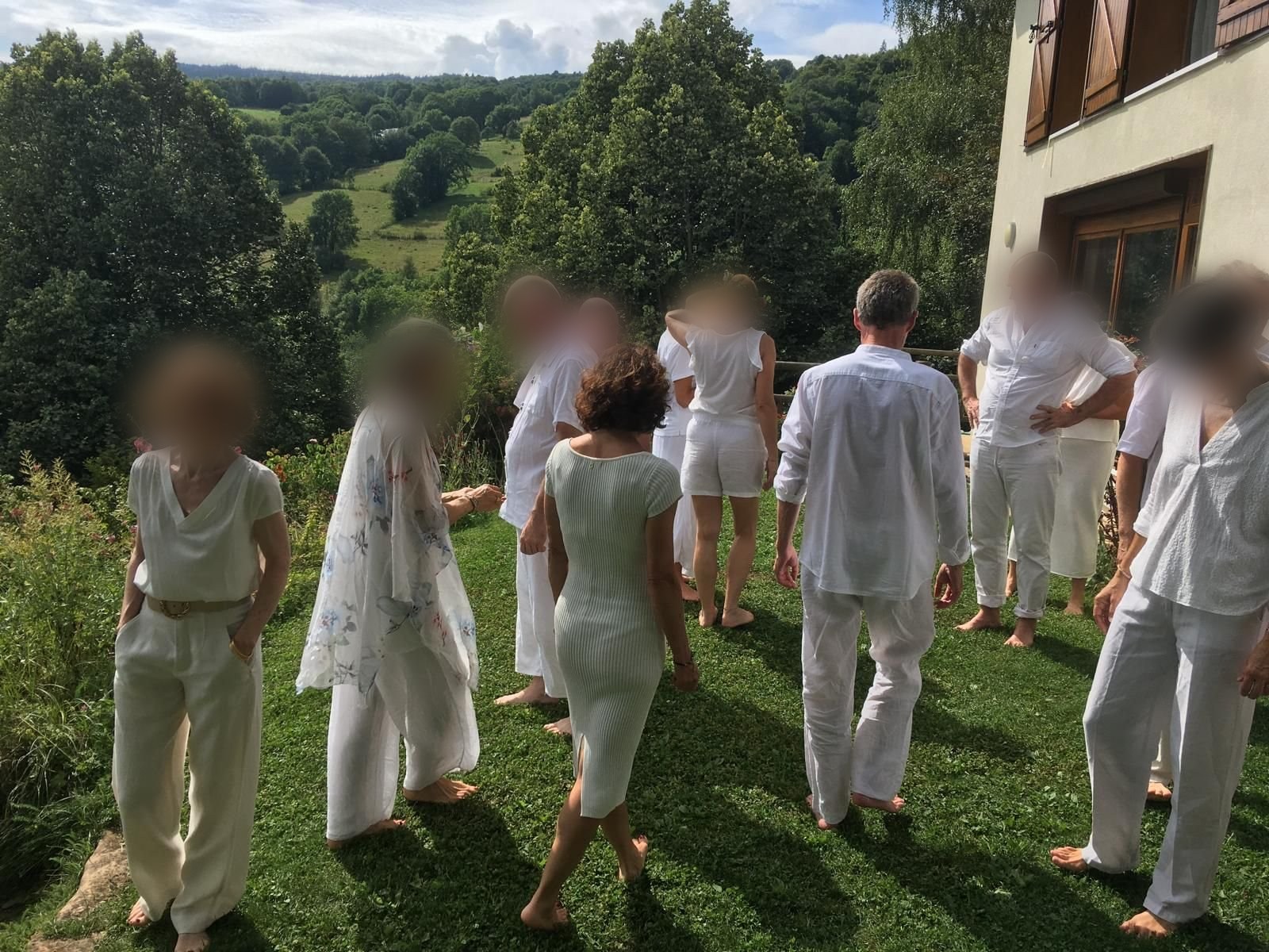 Grupo vestido de blanco, descalzo sobre el césped, con un valle arbolado de fondo
