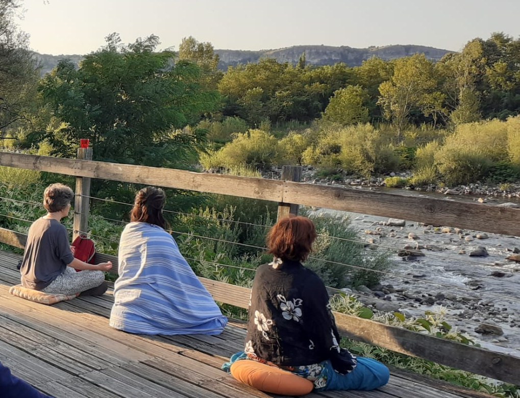 Personas meditando de espaldas frente a un río, al atardecer